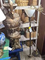 Photo showing the large decorative floor vase and two floor lamps together in storage environment with shelf and baskets in background.
