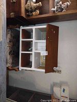 Wooden dollhouse showing three floors and multiple rooms with aged paint and wood floors, sitting on a cushioned bench.