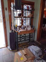 Baker's rack next to door with general view of rack and some items on shelves, showing metal frame and wooden shelves with drawers.