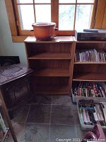 First wood bookcase empty, standing beside a wood stove and a pot on top of it.