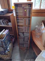 Tall narrow wooden CD cabinet with glass front door, filled with multiple rows of CDs.