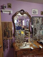 Mirror mounted on a purple wall above a wooden dresser with the detailed carved frame visible.