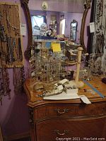 Wide view of dresser with mirror showing various jewelry pieces displayed including earrings, cuff links, bracelets, and belts on stands and laid on the surface.