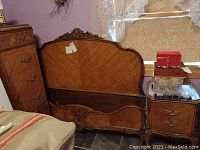 Wide view showing the full wooden headboard with decorative carving, footboard, metal bed frame, and adjacent nightstand with two drawers.