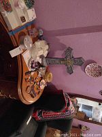 Wide shot of room with decorative crosses, jewelry sets in ring boxes, and assorted keys arranged on table against textured purple wall
