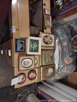Wide shot showing fourteen small framed wall art pieces arranged on a wood surface next to furniture and fabric items in the background.