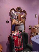 Full view of the ornate wall mirror mounted on a purple wall above an armchair with a decorative textile.
