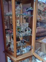 Photo of wooden and glass display cabinet with multiple crystal and glass decorative pieces including a broken Pegasus, mushroom glass, and floral ceramics.