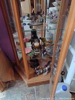 Wide view inside wooden glass display cabinet showing multiple figurines including birds, flowers, and various glass pieces.