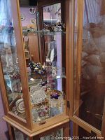 Wood framed glass display cabinet holding various figurines inside with cream colored ceramic floral pieces and crystal animals
