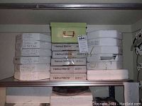 Stack of white styrofoam boxes containing collector plates alongside one green storage box on a metal shelf.