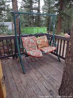 Green metal porch swing with floral cushions on a wooden deck