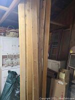 Long vertical wood boards leaning against wall in shed with various furniture and storage items nearby.