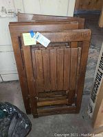 Six wood folding chairs stacked and folded flat, showing front and back slatted wood.