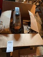 Top view of vintage KitchenAid mixer inside a cardboard box showing control knob and part of power cord.