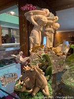 Glass and ceramic figurines including a cherub holding a bowl, two unicorn figurines, and additional glass decor on a glass shelf.