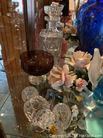 Clear crystal decanter, purple glass bowl, cut crystal bird figurines, ceramic pink rose flowers on glass shelf