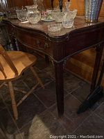 Side view of the vintage wood table showing carved leg and ornate faux drawer front.