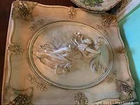 Close-up of plaster wall plaque with ornate corners and classical female figure relief