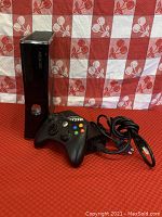 Xbox 360 console with wired controller and power cable shown on red and white checkered background.