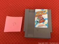 Front view of NES Super Mario Bros 2 game cartridge on red background with a handwritten numbered sticky note.