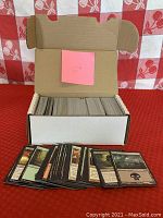 Open cardboard box filled with approximately 400 black border Magic cards, with several cards fanned out in front showing different card types and artwork.