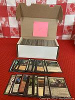 Open white box with approximately 400 loose Magic the Gathering black border cards inside. Front row cards spread out to show variety including creature and land cards.
