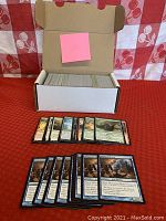 Open white cardboard storage box filled with approximately 400 unsorted Magic: The Gathering black border cards, with some cards fanned out in front.