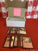 White storage box filled with approximately 400 loose Magic the Gathering black border cards. Sample cards laid in front showing various card art and text.