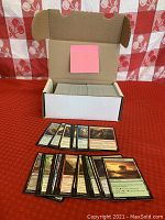 Photo of a white open storage box containing approximately 400 Magic The Gathering cards with black borders, with a variety of cards laid out in front showing a representative sample.