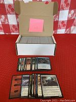 Open white cardboard storage box full of approximately 400 loose Magic the Gathering black border cards. A pink sticky note with '143' is placed inside the box.