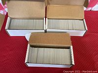 Three white cardboard boxes filled with trading cards on red tablecloth
