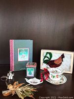 Photo showing the teacup, saucer, tea bag holder in dove shape, tea tin with Christmas tree design, "A Cup of Christmas Tea" book, silver plated angel salt and pepper shakers, dried corn husk decoration, and a stained glass rooster plaque in a box.