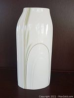 Tall white ceramic vase with sage and gold cypress tree motif photographed against a dark background.