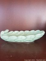 Side view of sea-foam green shell-shaped console dish on wooden surface against dark purple wall.