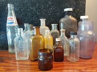 Front view showing assortment of 15 antique and vintage glass bottles and jars in various colors and shapes, including Pepsi-Cola bottle with label.