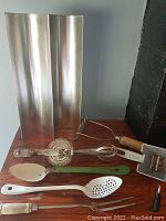 Full view of all items in lot including bread pans, manual beaters, spatula, spoons, and kitchen grater.