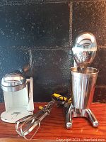 Photo of the Hamilton Beach Drink Master milkshake mixer with chrome design and metal mixing cup on wooden surface against black wall.