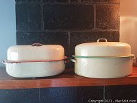 Two vintage enameled roasting pans side by side with lids, showing exterior wear and color differences.