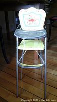 Front view of child's metal toy high chair showing painted reindeer design on backrest, green seat and tray, and metal legs with red tips.