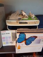 Canon ImageClass MF3240 printer from the top view showing control panel, cables, user manual, and toner cartridges.