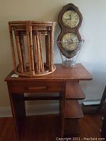 Solid wood desk with drawer and shelves, rattan nesting tables stacked on top, modern metal wire bin, Bulova clock and barometer on desk surface