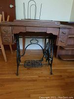 Front view of the full sewing machine cabinet showing wooden drawers and cast iron treadle base with detailed wrought iron design.