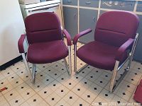 Front side view showing both burgundy upholstered chairs with chrome frames on vinyl tile floor next to kitchen cabinets.