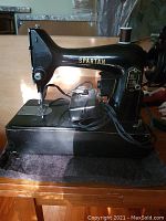 Side profile of black metal Singer Spartan sewing machine showing compact design and real wood table base.