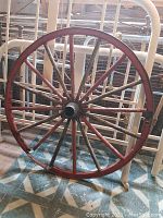 Front view of the wagon wheel showing full circle, the red wooden rim and spokes with central metal hub.