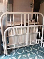 Full view of white tubular steel bed frame with headboard and footboard, showing overall structure and condition.