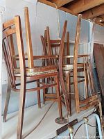 Four vintage wooden chairs stacked and leaning against a wall in a basement area, showing their structure and removable seats.