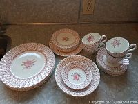 Full set of Johnson Bros. Rose Bouquet dishes, cups, and saucers on a counter, showing floral pink and red rose pattern with ruffled edges on plates