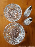 Overhead photo of two heavy pinwheel cut crystal ashtrays and two crystal salt and pepper shakers with silver caps